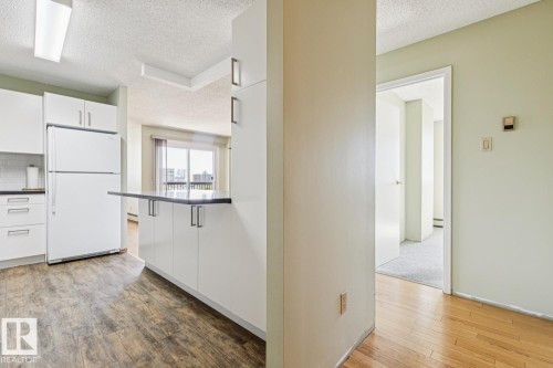 Kitchen with white cabinetry, dark countertops, and wood-finish flooring - #905 9929 113 St Nw, Edmonton, AB 