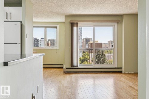 Hardwood flooring, sliding glass door leading to a balcony, white refrigerator, white cabinetry, and a window with urban scenery - #905 9929 113 St Nw, Edmonton, AB 