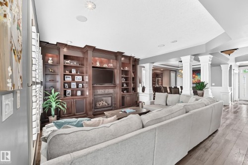 Built-in dark wood cabinetry with integrated lighting, gas fireplace with tile surround, engineering flooring, recessed lighting, and decorative columns - 417 Caldwell Place Nw, Edmonton, AB 