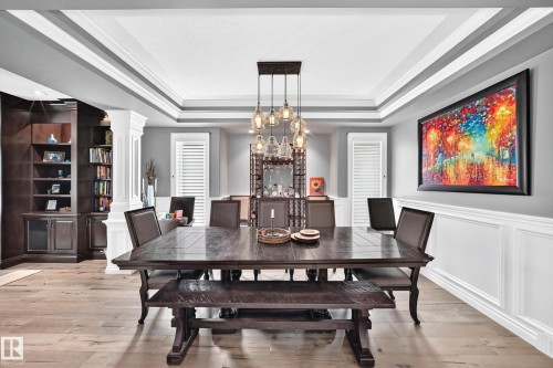 Tray ceiling with crown molding, built-in shelving, wainscoting, and a multi-pendant light fixture - 417 Caldwell Place Nw, Edmonton, AB 