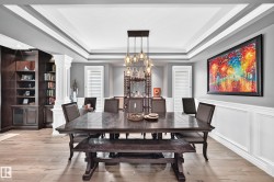 Tray ceiling with crown molding, built-in shelving, wainscoting, and a multi-pendant light fixture - 