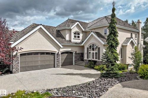 Stucco exterior with stone accents, multi-car garage, arched entry window with shutters, and mature landscaping - 417 Caldwell Place Nw, Edmonton, AB 