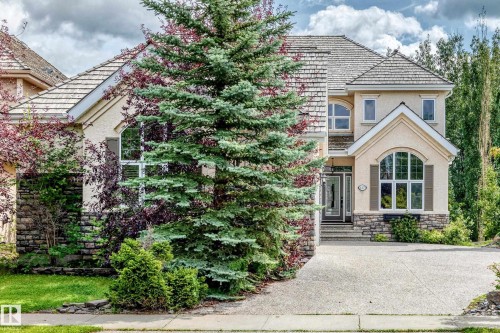 Elegant two-story residence featuring a cream and stone exterior with architectural detailing, arched entryway, and multi-pane windows - 417 Caldwell Place Nw, Edmonton, AB 