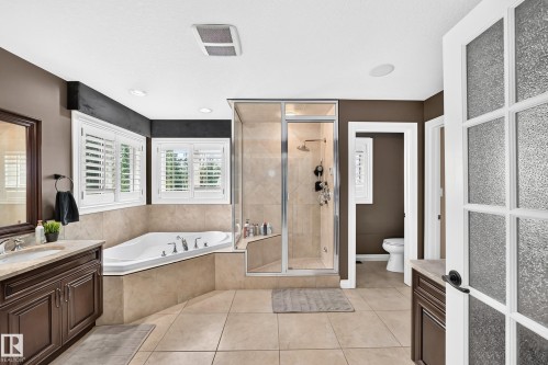 Recessed tub with tile surround, glass-enclosed shower, dual vanity with undermount sinks, plantation shutters, and tile flooring - 417 Caldwell Place Nw, Edmonton, AB 