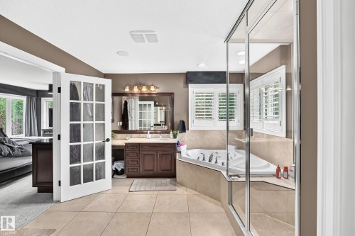 Soaking tub with tiled surround, separate glass-enclosed shower, dual-sink vanity with wood-finish cabinetry, and tiled flooring - 417 Caldwell Place Nw, Edmonton, AB 