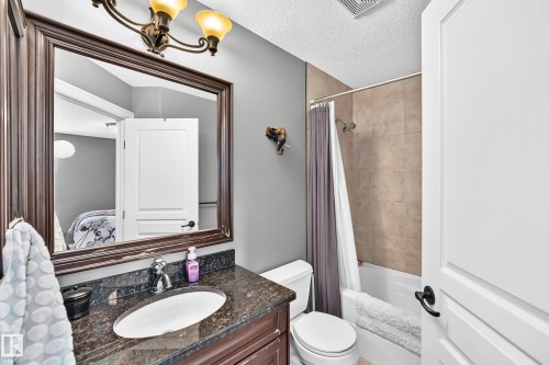 Bathroom featuring a single vanity with stone countertop, mounted sink, and an overhead bronze-tone light fixture - 417 Caldwell Place Nw, Edmonton, AB 