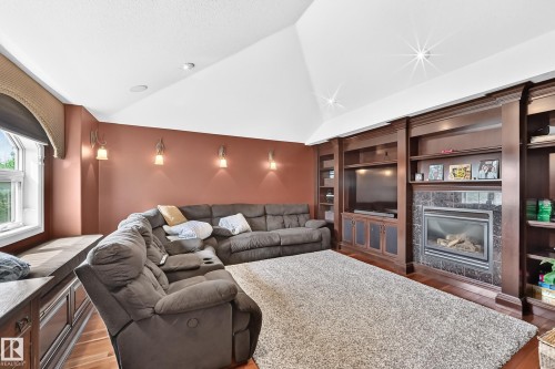 Vaulted ceiling, built-in media center with shelving, recessed lighting, wall sconces, and a gas fireplace with a dark stone surround - 417 Caldwell Place Nw, Edmonton, AB 