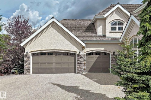 Stucco exterior with stone accents, two arched garage doors, a dormer window - 417 Caldwell Place Nw, Edmonton, AB 
