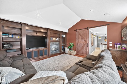 Vaulted ceiling, built-in entertainment center, fireplace with tile surround, and a sliding barn door - 417 Caldwell Place Nw, Edmonton, AB 
