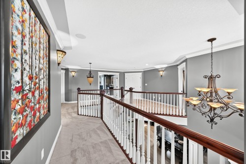 Expansive upper landing featuring plush carpeting, elegant white balusters with wood-finish handrails, decorative sconces, and a multi-tiered chandelier - 417 Caldwell Place Nw, Edmonton, AB 