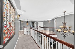 Expansive upper landing featuring plush carpeting, elegant white balusters with wood-finish handrails, decorative sconces, and a multi-tiered chandelier - 