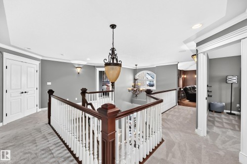 Carpeted landing featuring a dark wood and white baluster railing, an ornate chandelier, recessed lighting, and wall sconces - 417 Caldwell Place Nw, Edmonton, AB 