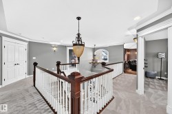 Carpeted landing featuring a dark wood and white baluster railing, an ornate chandelier, recessed lighting, and wall sconces - 
