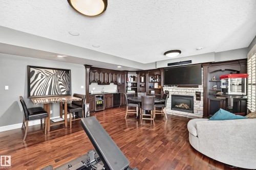 featuring a built-in wet bar with sink and cabinetry, built-in entertainment center with shelving, and a gas fireplace with stone surround - 417 Caldwell Place Nw, Edmonton, AB 