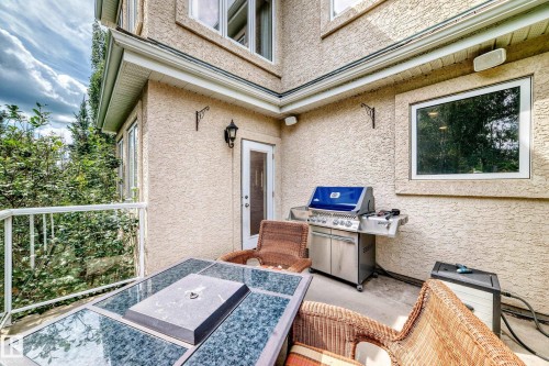 Outdoor patio area with textured stucco exterior, white railing, and exterior lighting fixtures - 417 Caldwell Place Nw, Edmonton, AB 