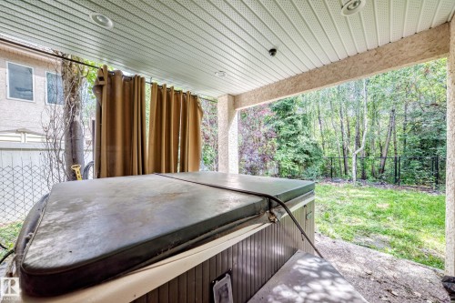 Covered patio featuring a hot tub and an expansive grassy area surrounded by mature trees - 417 Caldwell Place Nw, Edmonton, AB 