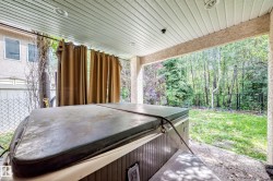 Covered patio featuring a hot tub and an expansive grassy area surrounded by mature trees - 