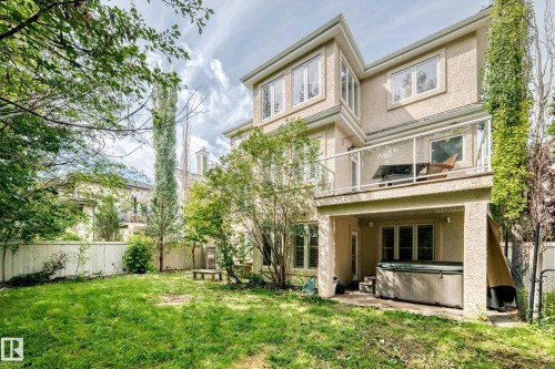 Stucco exterior with multiple windows, upper-level glass-paneled deck, lower-level covered patio, built-in hot tub, and fenced yard - 417 Caldwell Place Nw, Edmonton, AB 