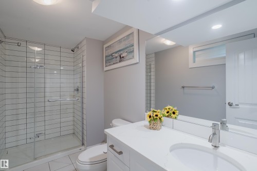 Glass-enclosed shower with subway tile surround, single vanity with integrated sink, polished chrome faucet, and expansive wall-mounted mirror - 4708 106 Avenue Nw, Edmonton, AB 