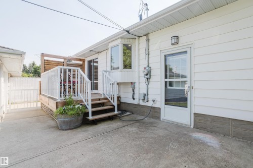 Exterior white siding with a ground-level concrete patio, a raised wood deck with white railings, and a glass-paneled exterior door - 4708 106 Avenue Nw, Edmonton, AB 