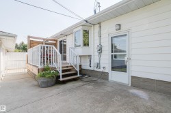Exterior white siding with a ground-level concrete patio, a raised wood deck with white railings, and a glass-paneled exterior door - 