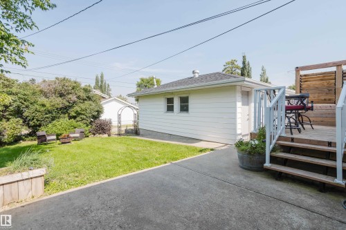 Backyard featuring a wood deck with steps, a detached structure with white siding, a concrete driveway, and a grass lawn with mature landscaping - 4708 106 Avenue Nw, Edmonton, AB 
