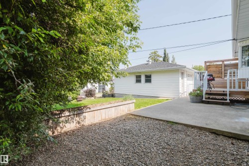 Gravel parking area with a wood-retaining wall, leading to a concrete patio and a raised wood deck - 4708 106 Avenue Nw, Edmonton, AB 