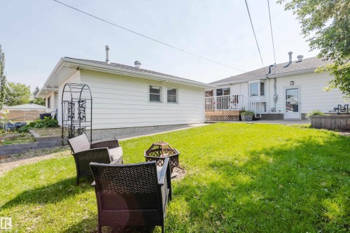 Expansive grassy area with a wooden deck, raised garden bed, and white siding exterior - 4708 106 Avenue Nw, Edmonton, AB 