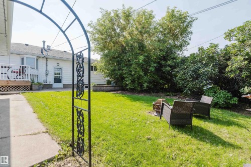 Expansive green lawn, mature perimeter trees, concrete walkway, decorative metal archway, and raised garden bed - 4708 106 Avenue Nw, Edmonton, AB 