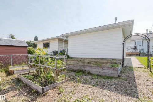 Raised garden beds, arched metal garden entry, cement walkway, and white siding exterior - 4708 106 Avenue Nw, Edmonton, AB 