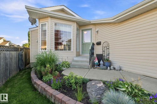 Bay window with grid accents, light beige siding, concrete pathway, brick-edged garden bed, and a light green entry door - 30 Belfry Fairway Crescent, Stony Plain, AB 