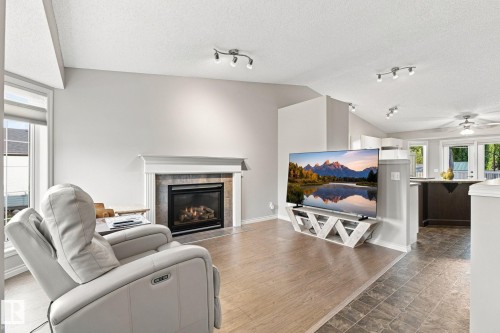 Living area featuring a fireplace with a stone surround and mantel, vaulted ceilings, track lighting, and wood-finish flooring - 30 Belfry Fairway Crescent, Stony Plain, AB 