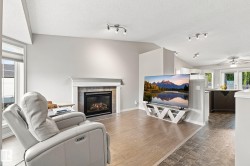 Living area featuring a fireplace with a stone surround and mantel, vaulted ceilings, track lighting, and wood-finish flooring - 