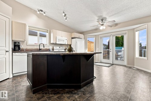 Kitchen featuring a center island, light-toned cabinetry, white appliances, and a vaulted ceiling with track lighting - 30 Belfry Fairway Crescent, Stony Plain, AB 