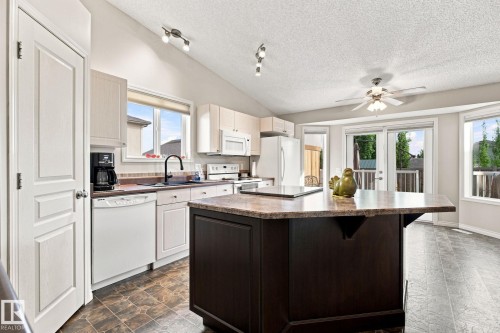 Kitchen featuring light-toned cabinetry, a dark-toned island with a light-toned countertop, a ceiling fan, and patio doors - 30 Belfry Fairway Crescent, Stony Plain, AB 