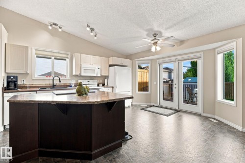 Kitchen with vaulted ceiling, track lighting, a center island with a stone-finish countertop, and white cabinetry - 30 Belfry Fairway Crescent, Stony Plain, AB 