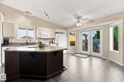 Kitchen with vaulted ceiling, track lighting, a center island with a stone-finish countertop, and white cabinetry - 