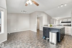 Open-concept living area featuring a kitchen island with storage, track lighting, a ceiling fan, and tiled flooring - 