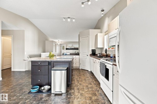 Kitchen featuring a central island with countertop seating, dark wood-finish cabinetry, white appliances, and track lighting - 30 Belfry Fairway Crescent, Stony Plain, AB 