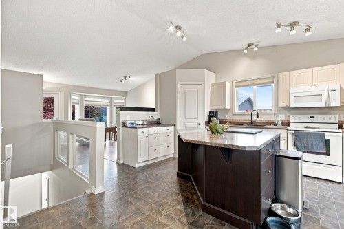 Kitchen featuring a central island with stone-finish countertop, white appliances, and track lighting - 30 Belfry Fairway Crescent, Stony Plain, AB 