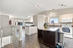 Kitchen featuring a central island with stone-finish countertop, white appliances, and track lighting - 