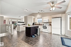 Spacious kitchen featuring white appliances, a center island with a dark wood-finish base, ample cabinetry, and a ceiling fan - 