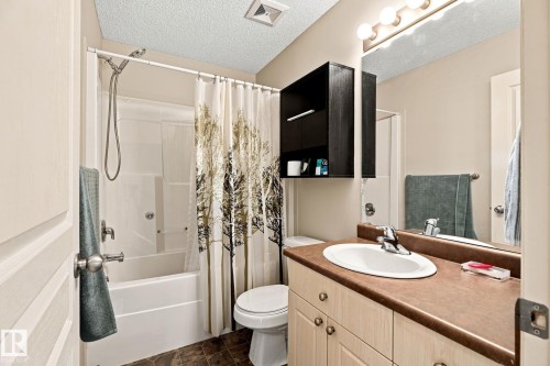 Vanity with integrated sink and brown countertop, wall-mounted mirror with overhead lighting, white tub/shower combination, and dark wood-finish wall cabinet - 30 Belfry Fairway Crescent, Stony Plain, AB 