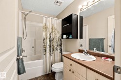 Vanity with integrated sink and brown countertop, wall-mounted mirror with overhead lighting, white tub/shower combination, and dark wood-finish wall cabinet - 