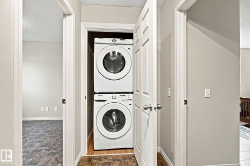 Stackable laundry appliances within a dedicated closet, featuring a paneled door and neutral wall tones - 30 Belfry Fairway Crescent, Stony Plain, AB 