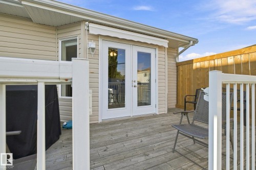 Expansive wood deck with white railing, featuring double French doors and an exterior wall light fixture - 30 Belfry Fairway Crescent, Stony Plain, AB 