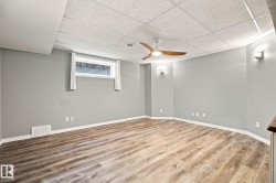 Wood-finish flooring, drop ceiling, modern ceiling fan, wall sconces, and a window - 