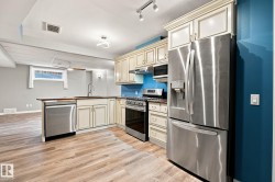 Kitchen featuring stainless steel appliances, wood-finish flooring, cream-colored cabinetry, a built-in microwave, and track lighting - 