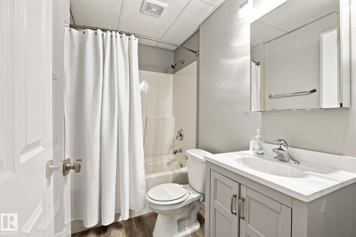 Full bathroom featuring a white bathtub/shower combination, light gray vanity with an integrated sink, polished chrome faucet, and wood-finish flooring - 30 Belfry Fairway Crescent, Stony Plain, AB 