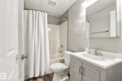 Full bathroom featuring a white bathtub/shower combination, light gray vanity with an integrated sink, polished chrome faucet, and wood-finish flooring - 